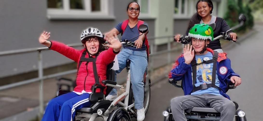 Foto von zwei Teilnehmenden der Ferienbetreuung, die mit zwei Mitarbeitenden mit dem Rollfiets unterwegs sind