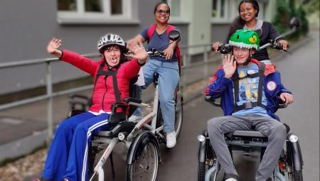 Foto von zwei Teilnehmenden der Ferienbetreuung, die mit zwei Mitarbeitenden mit dem Rollfiets unterwegs sind