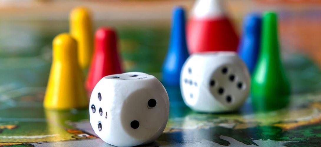 Bunte Spielfiguren und Würfel liegen auf einem Brettspiel